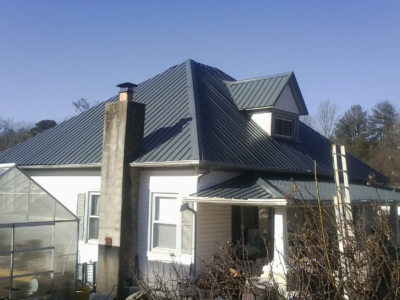 Dark blue standing seam metal roof on a white farmhouse with dormer — Slate & Tile Roof Repair by Roofing Brothers in Chattahoochee