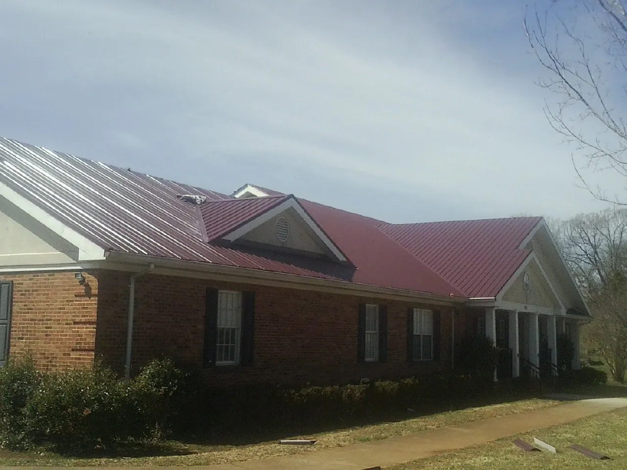 Red metal roof with gabled entries on a long brick building, from a Hail Damage Roof Repair job in Chattahoochee