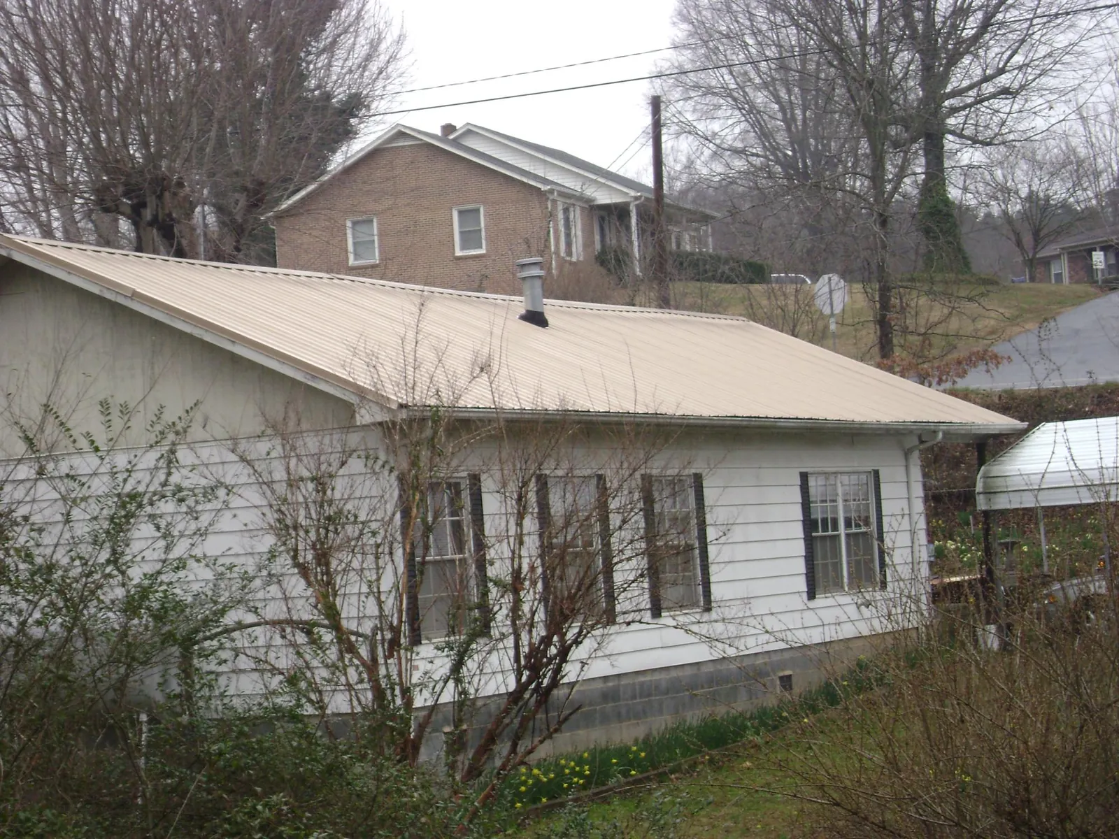 Tan metal roof on a white sided house set into a hillside — Commercial Roofing by Roofing Brothers in Chattahoochee